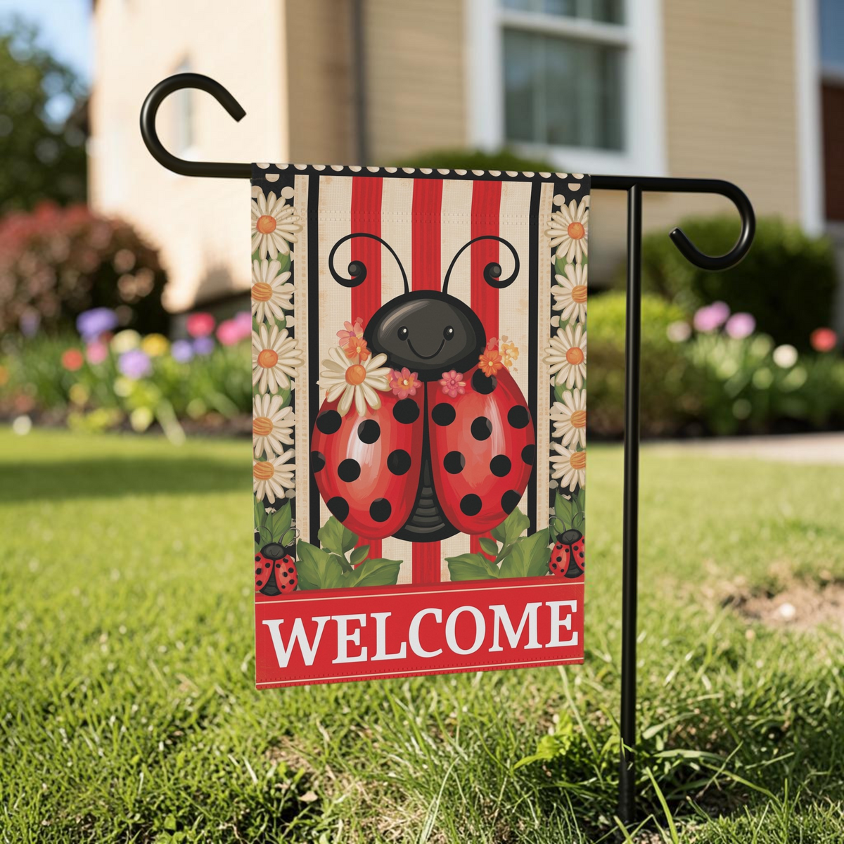 Welcome Ladybug garden flag on a black stand in a sunny front yard with a beige house and flowering shrubs