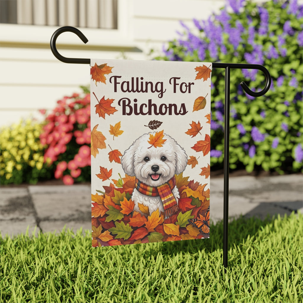 Close-up of the Falling For Bichons garden flag on its stand near a stone walkway with colorful flower bushes