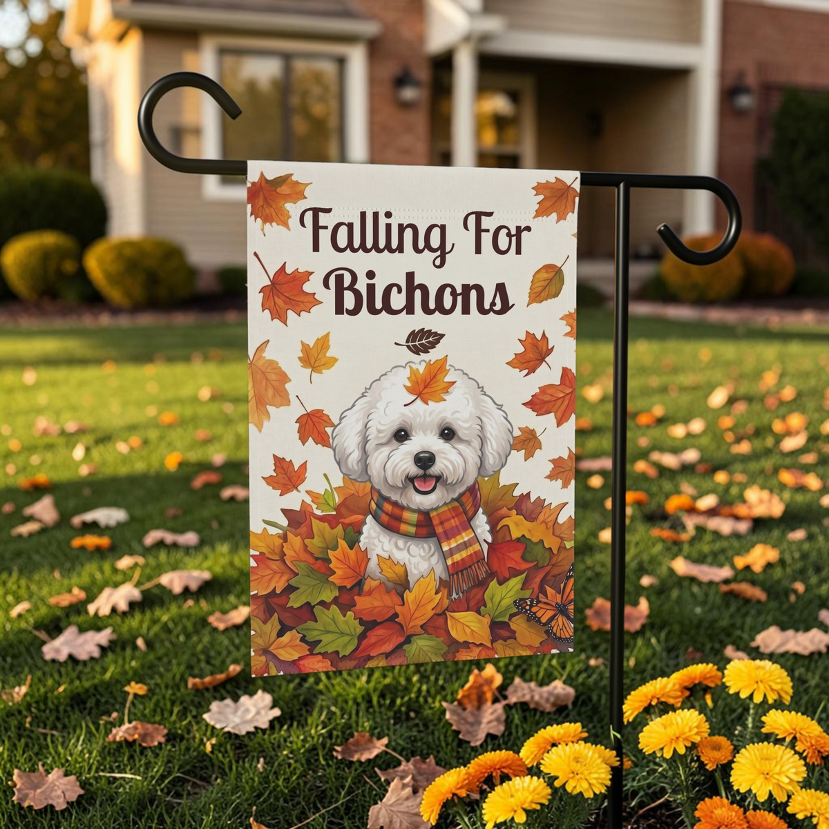 Falling For Bichons garden flag on its stand in front of a brick house with fallen autumn leaves on the grass