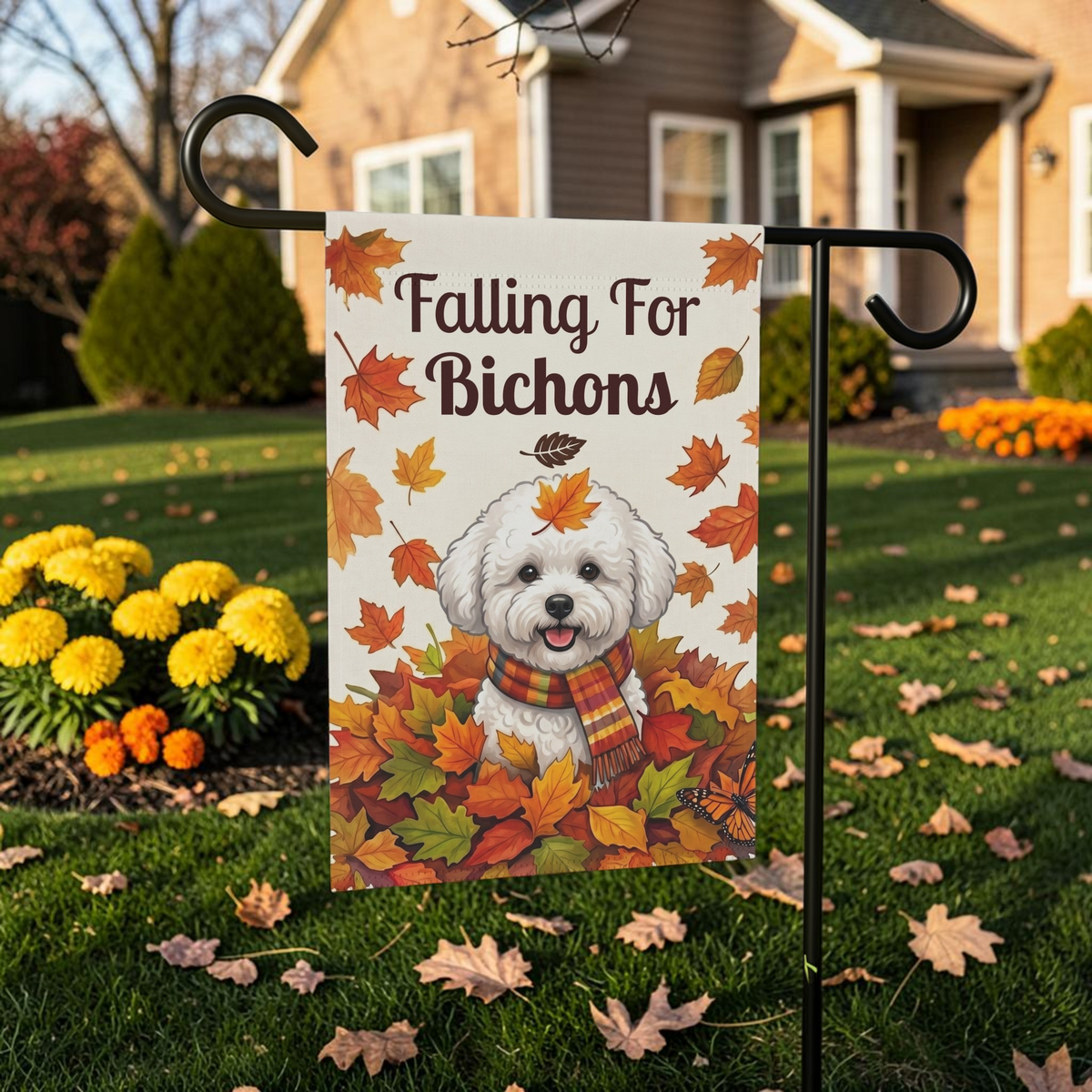 Falling For Bichons garden flag on a black stand on a leaf-covered lawn near yellow mums in a bright outdoor setting