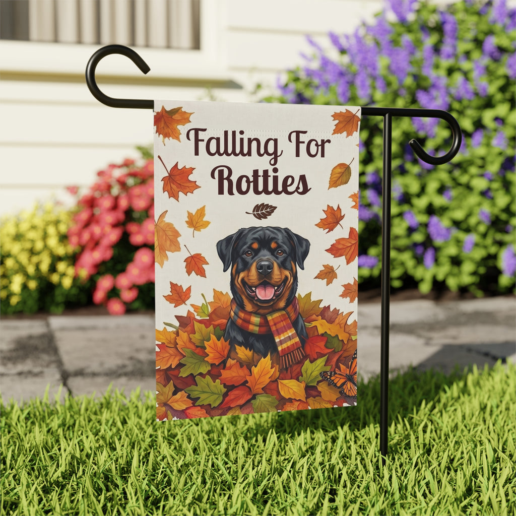Falling For Rotties Rottweiler garden flag on its stand near purple, pink, and yellow flowering bushes along a walkway