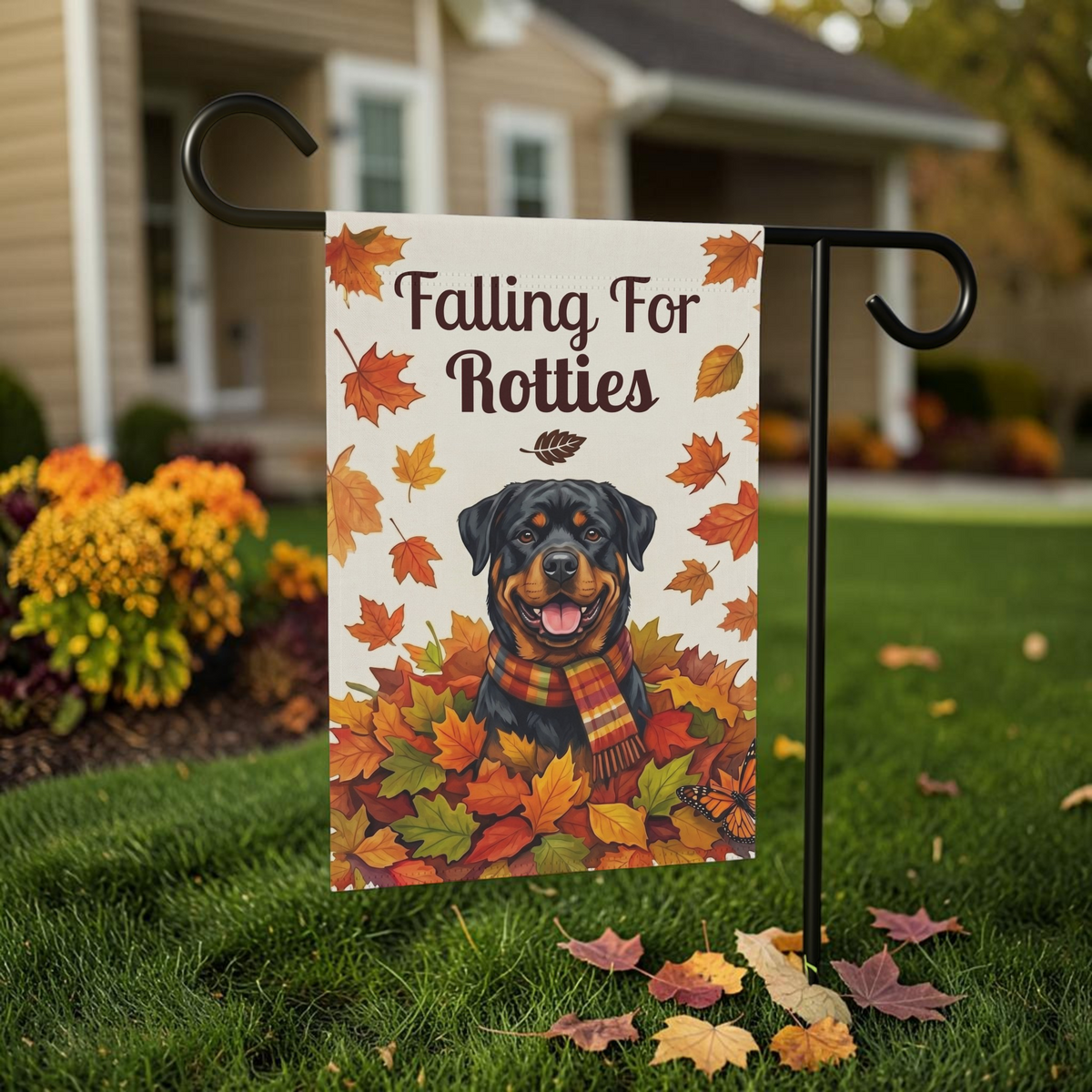 Falling For Rotties Rottweiler garden flag on a black stand in front of a house, showing the Rottweiler in a plaid scarf among autumn leaves and a monarch butterfly