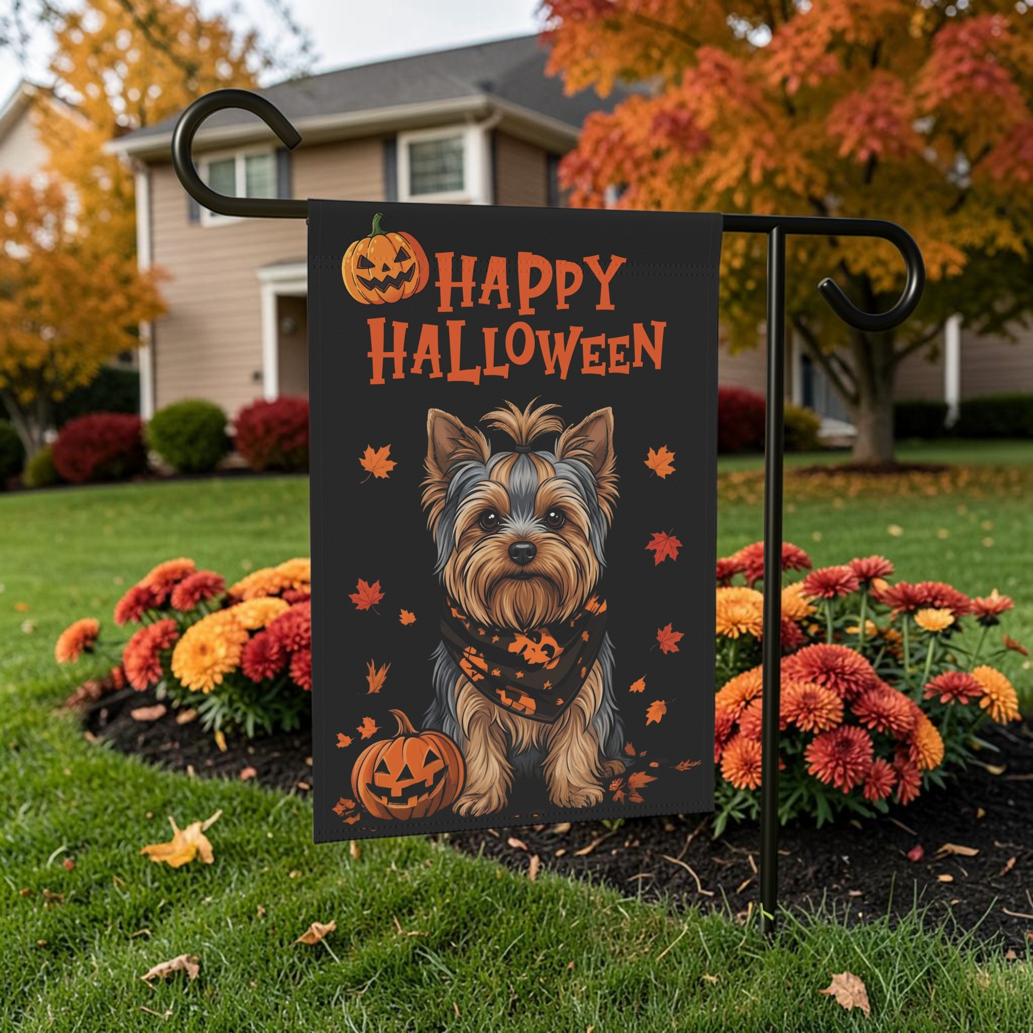 Little Pumpkin Yorkshire Terrier Halloween garden flag displayed on its stand among orange mums with an autumn tree in the background