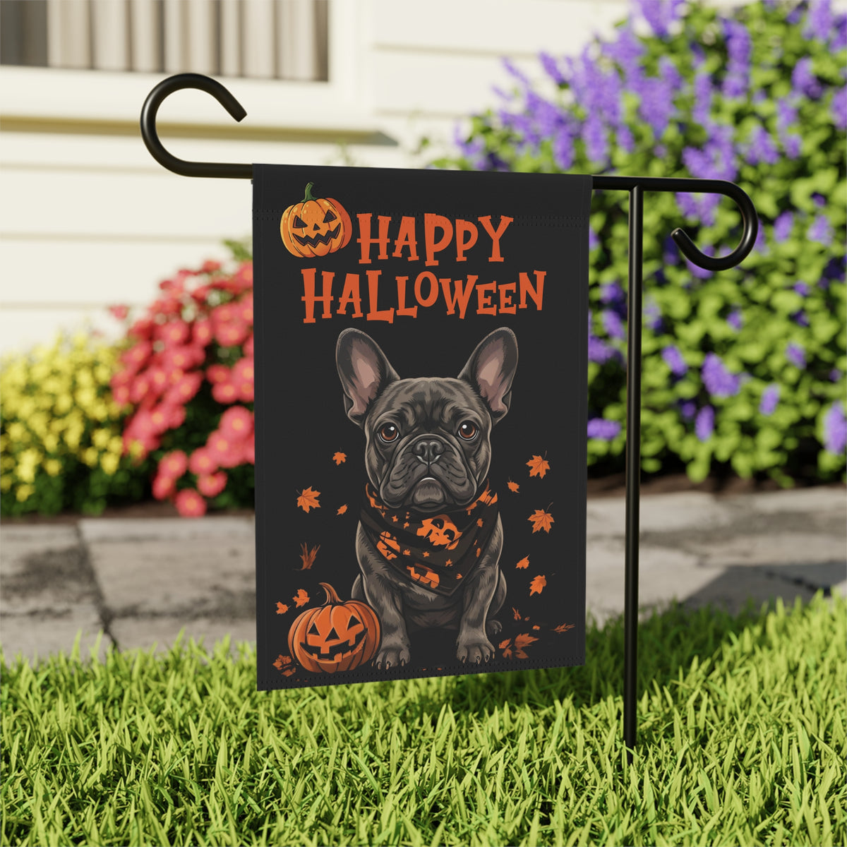 Little Pumpkin French Bulldog Halloween garden flag on a stand near a walkway lined with flowering shrubs