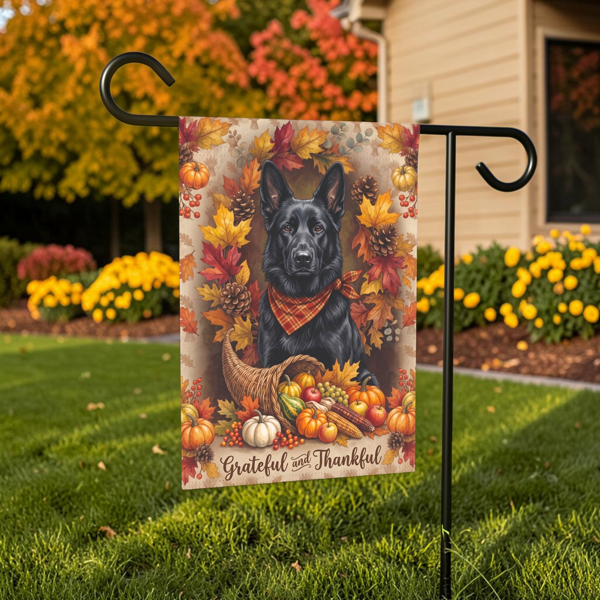 Grateful and Thankful Black German Shepherd garden flag displayed on a stand in a garden bed with autumn flowers and a house in the background