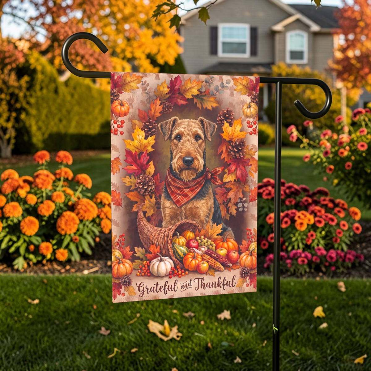 Grateful And Thankful Airedale Terrier garden flag displayed on a stand in a garden bed with autumn flowers and a house in the background